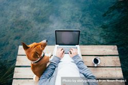 Man with coffee, dog and laptop sitting on the lake bYR7X0