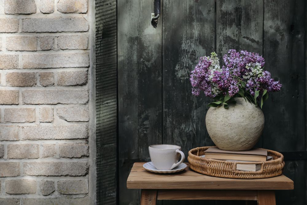 Lilacs, wicker tray, books against brick wall in sunlight