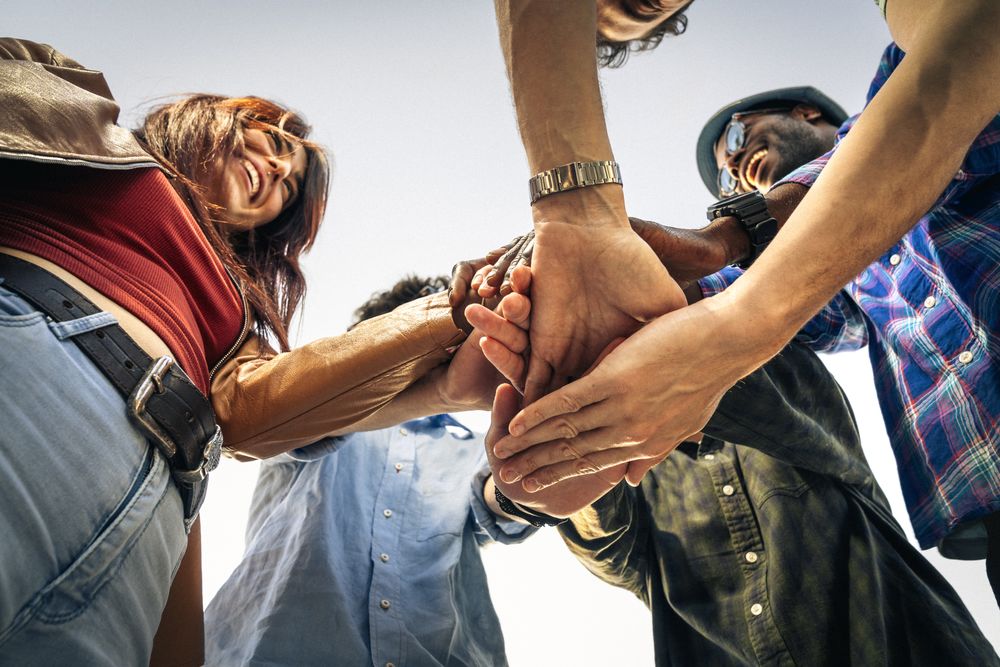 Low-angle view of a diverse group of friends stacking hands in a circle.