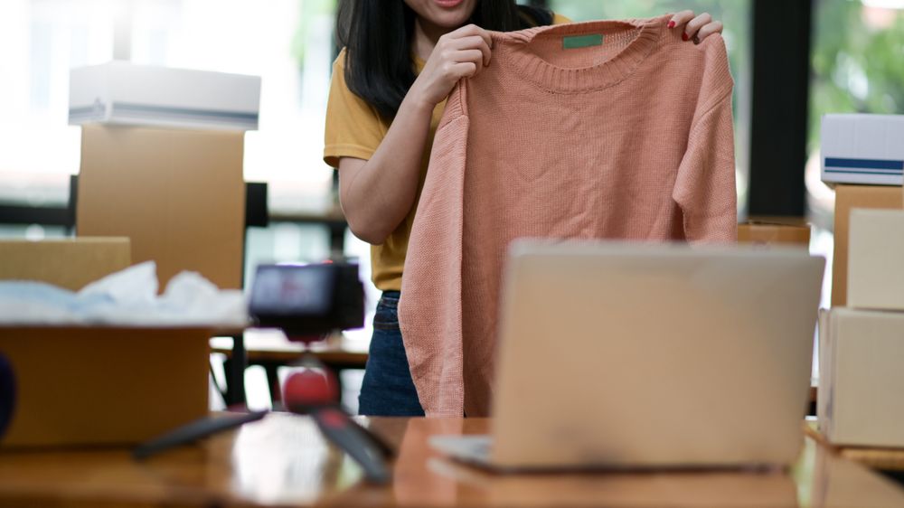 Women show selling shirts online from home. She uses her laptop to sell on social media