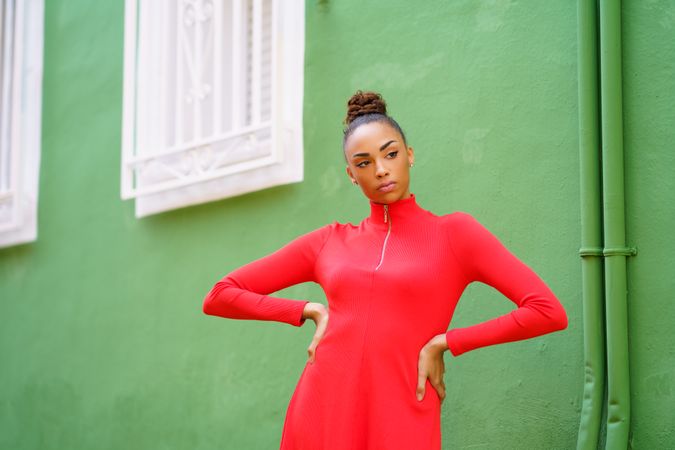 Serious female in red zipped up shirt standing outside green building