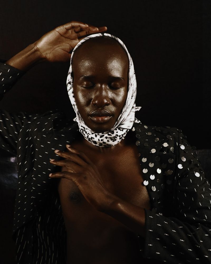 Bare-chested man wearing dark polka top and headscarf closing his eyes