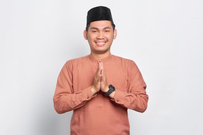 Muslim man in kufi hat smiling with hands closed in prayer