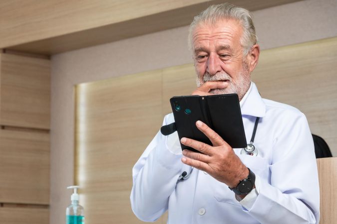Grey haired doctor checking notes phone