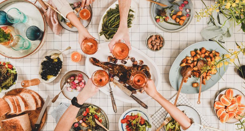 Flat-lay of peoples hands clinking with glasses of rose wine over table