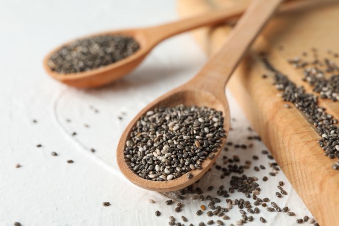 Wooden spoons with chia and board on plain background, close up