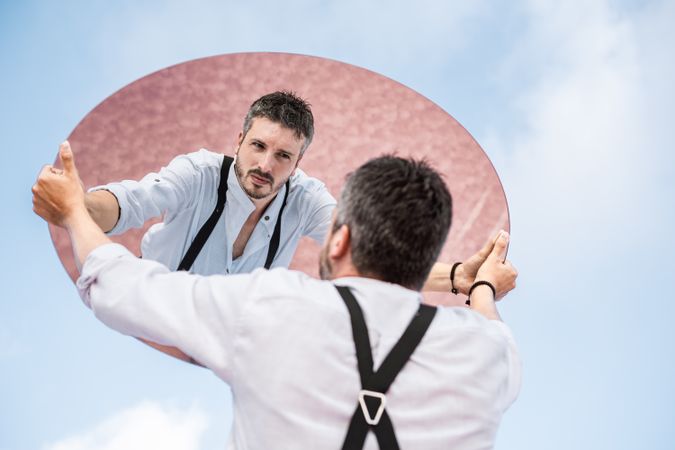 Stylish man holding mirror up and reflecting