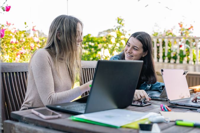 Two smiling female friends comparing their notes and chatting about what was written on the laptop.