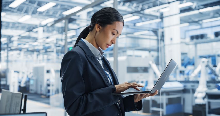 Portrait Of Electronics Manufacturing Technician Working on a Laptop Computer at a Factory Space. Asian Female Specialist Developing, Maintaining, and Fine-Tuning Programs for Production and Assembly.