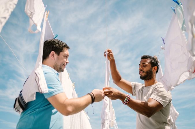 Multiracial men hanging clothes in bright day