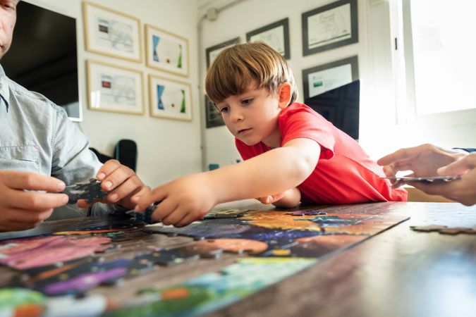 Preschooler solving jigsaw puzzle with faceless parents at home