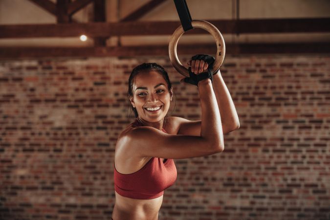 Fit woman holding gymnast rings at the gym and smiling