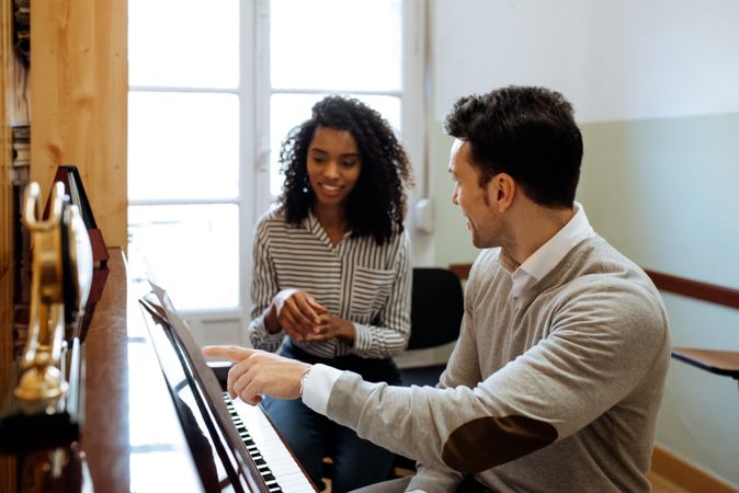 Man playing piano near woman teaching in studio