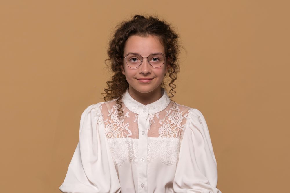 Girl with curly hair and glasses smiling, wearing lace blouse.