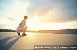 Woman crouching down with bright sunrise and cityscape in background 4dDxN4