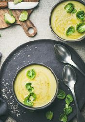Two bowls of Brussels sprout soup, on dark plate, garnished with fresh sprouts