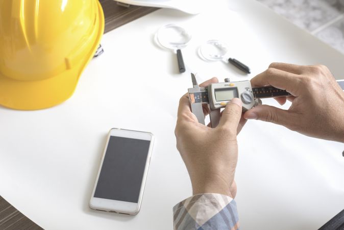 Person at work desk with hard hat, phone, magnifying glass and calipers