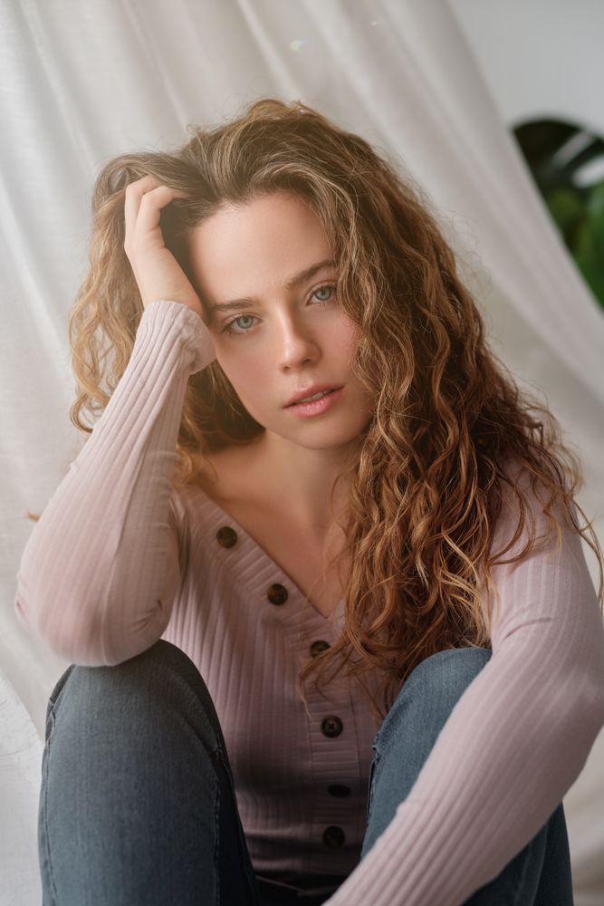 Charming woman sitting near curtain and daydreaming