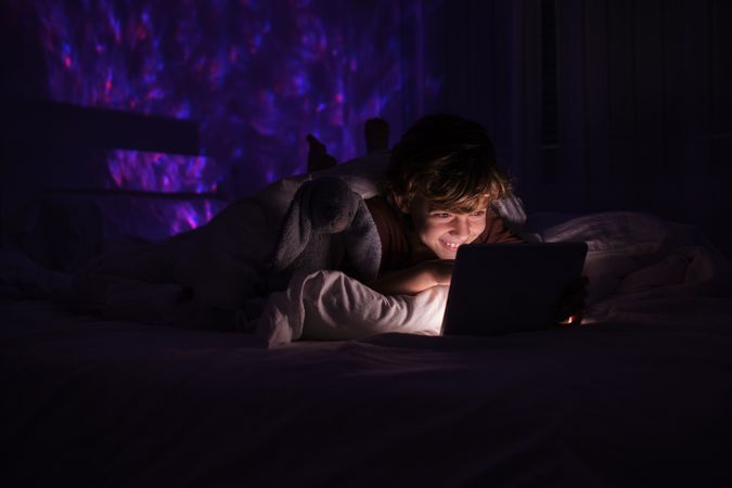 Happy boy watching video on tablet in dark bedroom