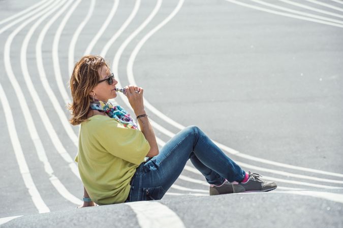 Modern relaxed woman vaping while sitting on marked road