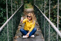 Happy female traveler taking selfie on suspension bridge in summer