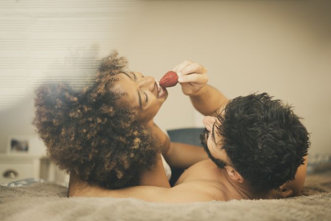Happy couple eating strawberry on bed