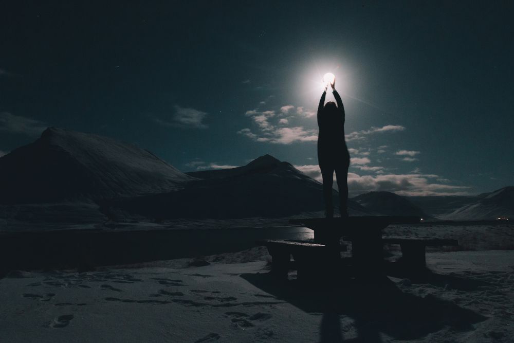 Woman on table on coast near water at night with moon in sky