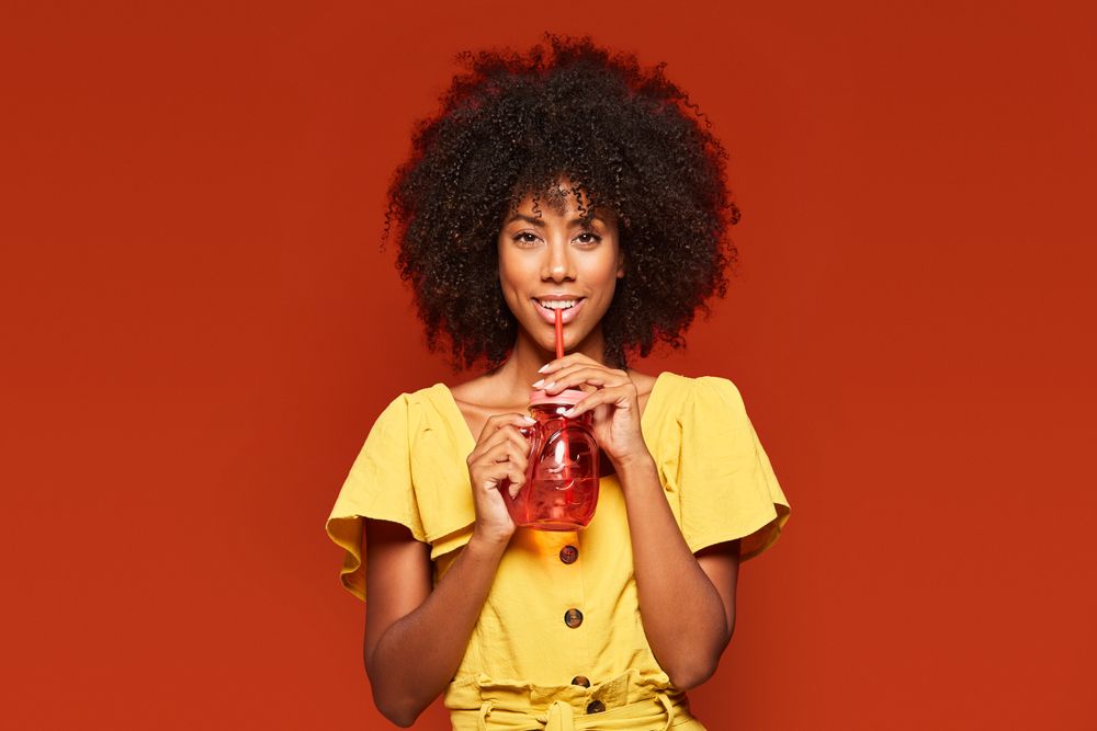 Charming bright Black woman drinking beverage