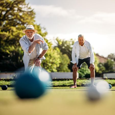 Older man playing boules in a playground with his playmate standing in the background