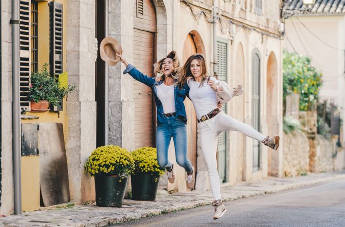 Friends having fun and jumping holding hands in street