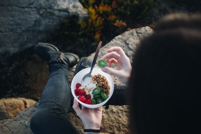 Woman holding kiwi from yogurt breakfast bowl