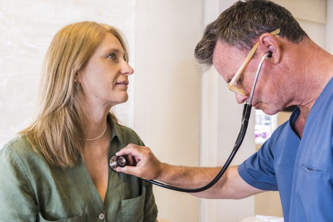 Adult doctor wearing scrub clothes checking her patient's heart beat with stethoscope.