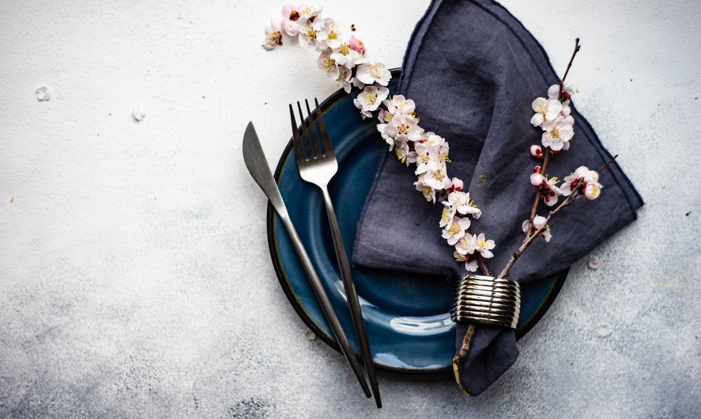 Table setting with delicate apricot blossom around elegant navy tableware on grey counter with space for text