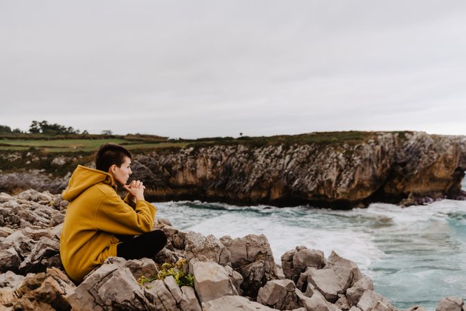 Woman in yellow hoodie on stony shore