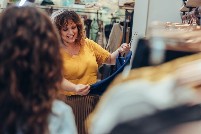 Female shopper talking with shop owner as she looks at dress