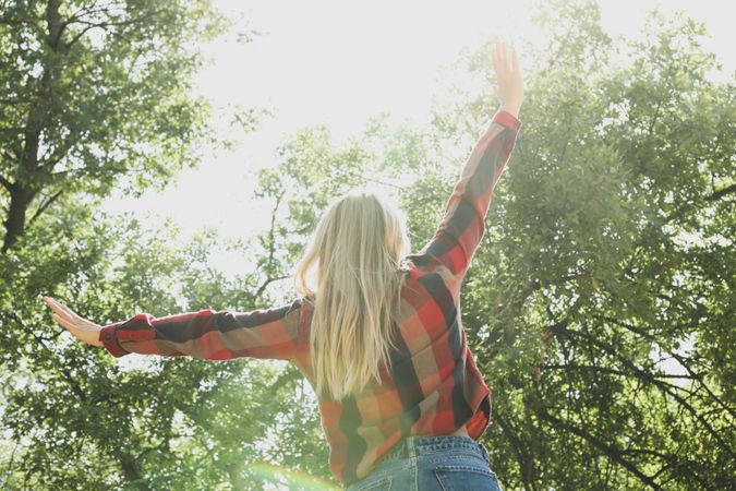 Happy woman in shirt and jeans with raised arms outdoor