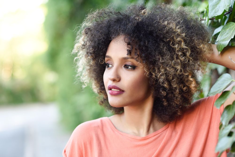 Portrait of wistful Black woman with afro hairstyle in front of wall with vines