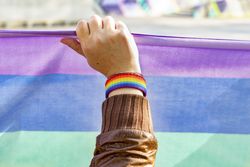 Close up of a woman arm with a LGBTQ rainbow wristband holding a Rainbow flag, concept of gay pride month, lesbian pride, LGBT awareness movement, non-binary inclusivity, and diversity