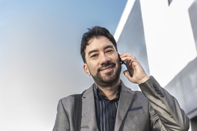 Low-angle view of an businessman talking on the cell phone while looking at camera in the street.