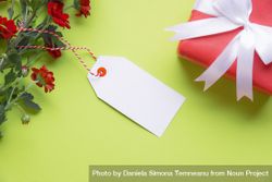 Top view of red flowers with blank gift tag and wrapped present 0Jxp84