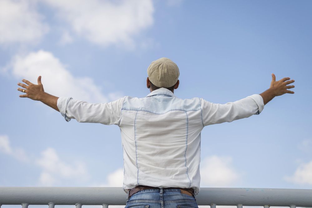Male in denim standing with open arms on sunny day
