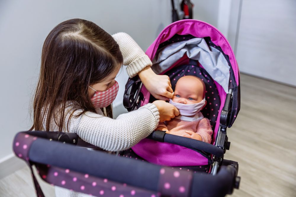 Girl with face mask putting mask on her baby doll