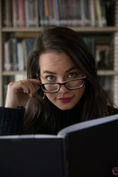 Woman in glasses standing along bookshelves and holding open book