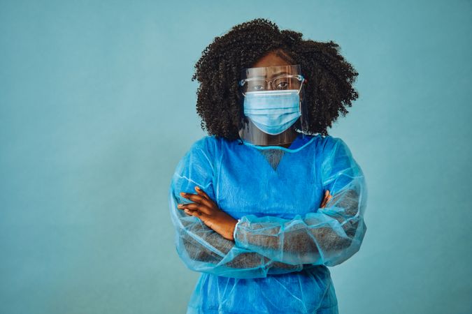 Serious Black female medical professional in surgical PPE, eye mask and shield, with arms crossed