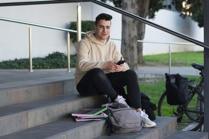 Young boy sitting on a campus steps while texting on phone