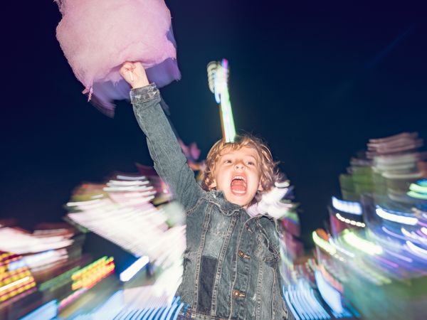 Excited boy with cotton candy screaming near attraction