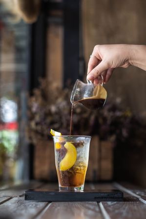 Person pouring coffee on orange garnished alcoholic cocktail