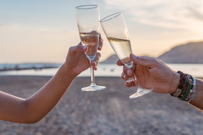 Crop women clinking wineglasses on beach during sunset