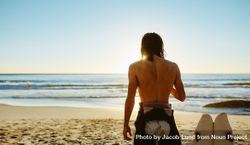 Rear view shot of young man standing on beach with surfboard bERPV0
