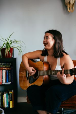 Young woman playing guitar laughing and looking away from camera